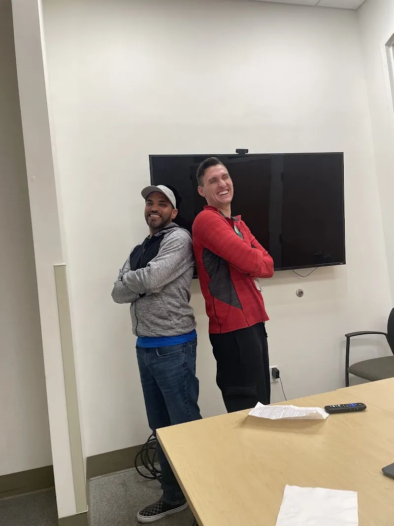 Two residents smiling back-to-back in a communal space at Riverbend, a sober living home in Boston.